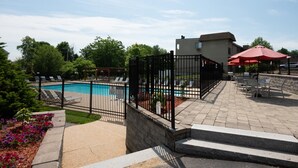 A swimming pool with a black fence, lounge chairs, and a red umbrella.