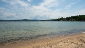 A beach with clear water, a sandy shore, and a distant shoreline with trees and houses.