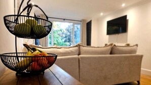 Una sala de estar moderna con una mesa de centro de madera, dos cestas de alambre negras para fruta, un sofá color beige y un televisor montado en la pared.