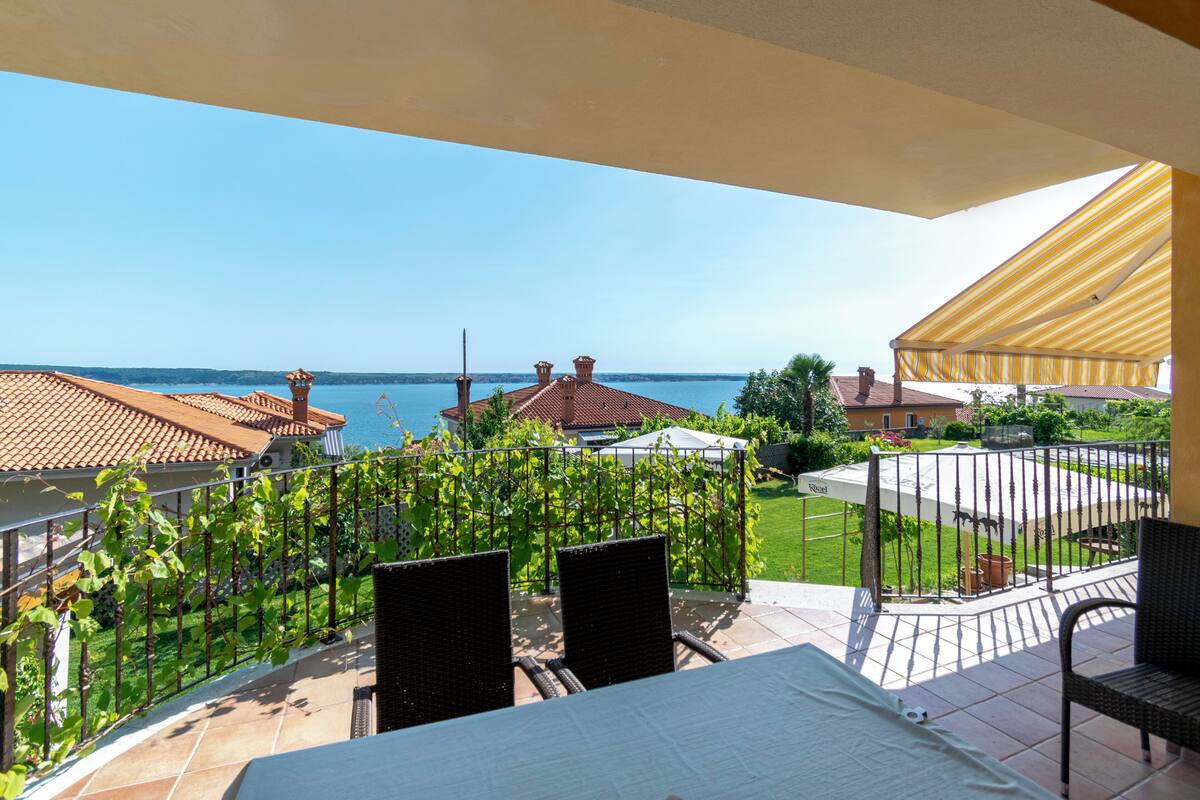 A balcony with a view of the sea, a covered patio, and a garden area.