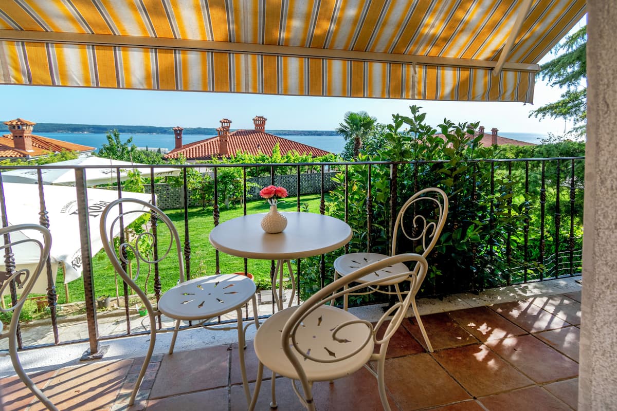 A terrace with a view of the sea, featuring a round table, two chairs, and a decorative vase.