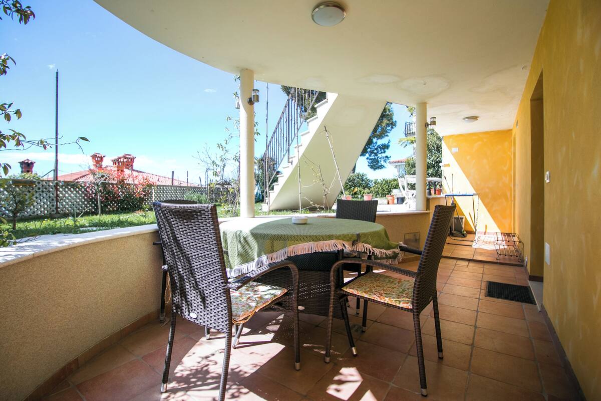 A covered patio with a table and chairs, a view of a building, and a yellow wall.