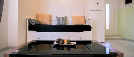 Une pièce moderne avec une table basse en verre, un canapé blanc agrémenté de coussins à motifs et une petite plante décorative.
