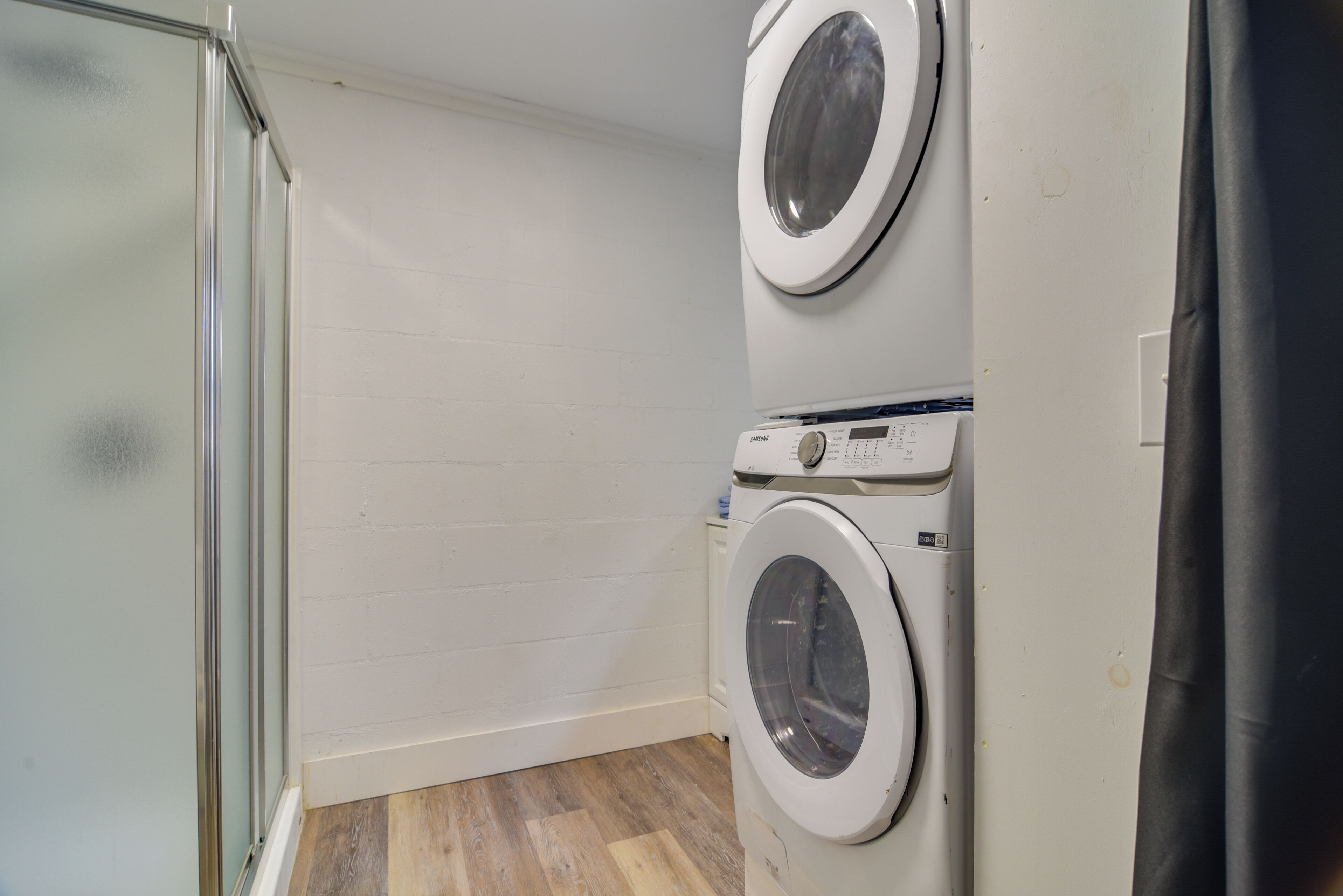 A laundry room with two stacked washing machines and a glass shower enclosure.