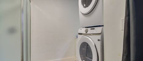 A laundry room with two stacked washing machines and a glass shower enclosure.