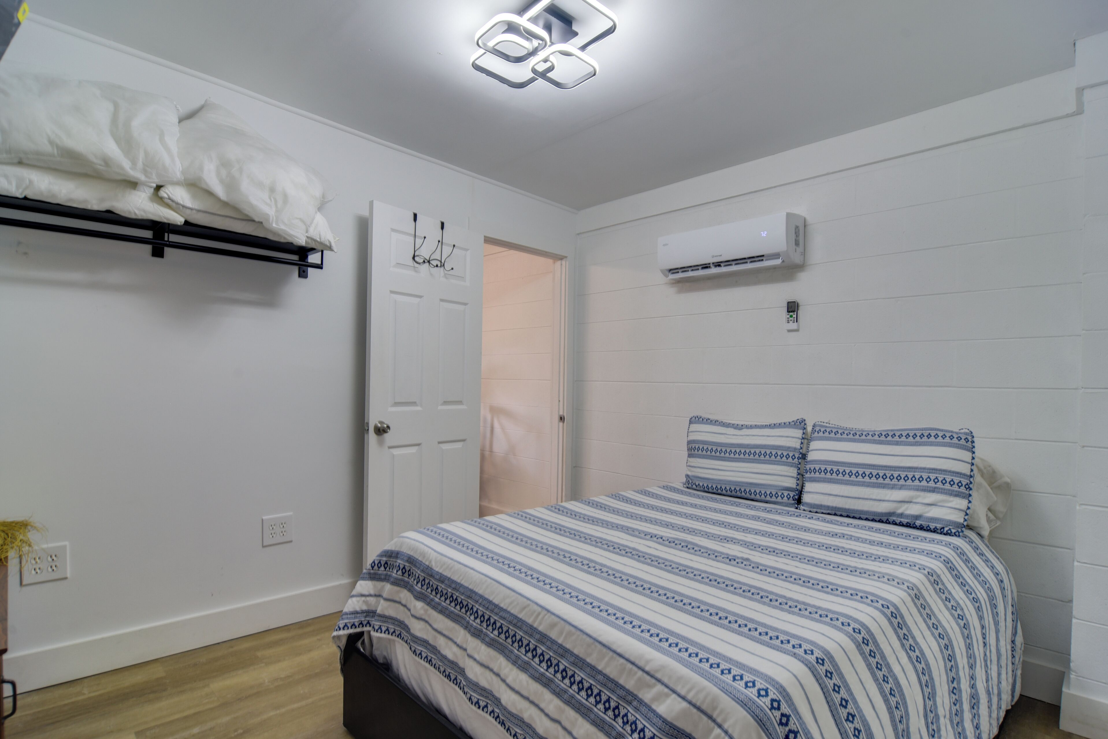 Una camera da letto con un letto, pareti bianche, una porta e un condizionatore.