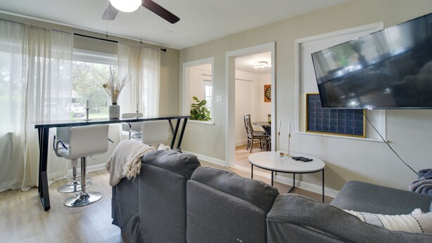 A modern living room with a ceiling fan, a flat-screen TV mounted on the wall, a dining area with a table and chairs, and a large grey sofa. - 13 Mi to Busch Gardens: Tampa Gem w/ Grill & Yard (Tampa)