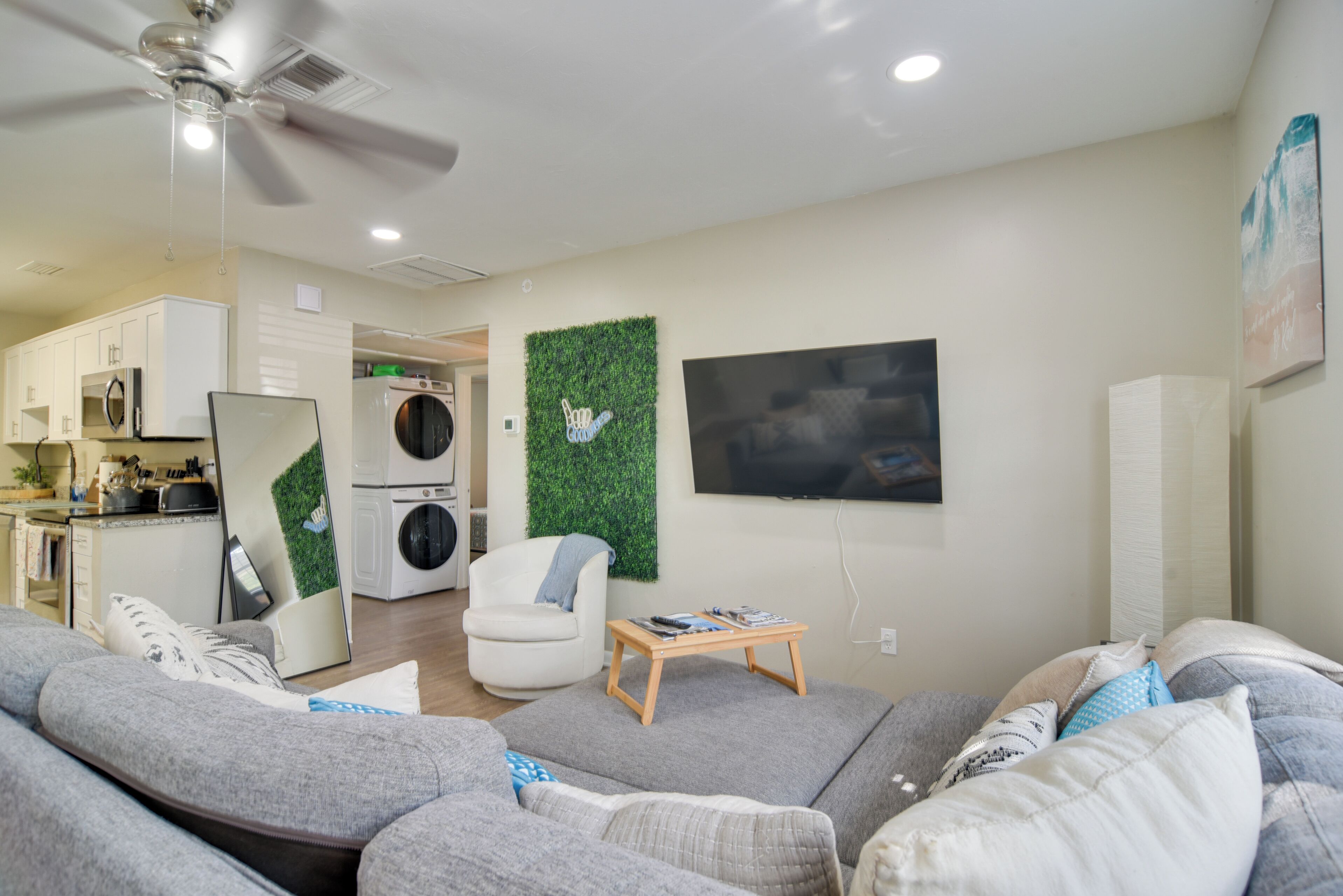 A modern living room with a grey sofa, a white armchair, a wooden coffee table, and a flat-screen TV mounted on the wall.