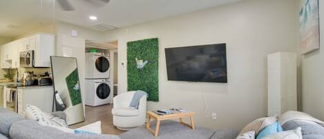 A modern living room with a grey sofa, a white armchair, a wooden coffee table, and a flat-screen TV mounted on the wall.