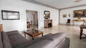 A spacious living room with a large grey sofa, a wooden coffee table, and a television mounted on the wall.
