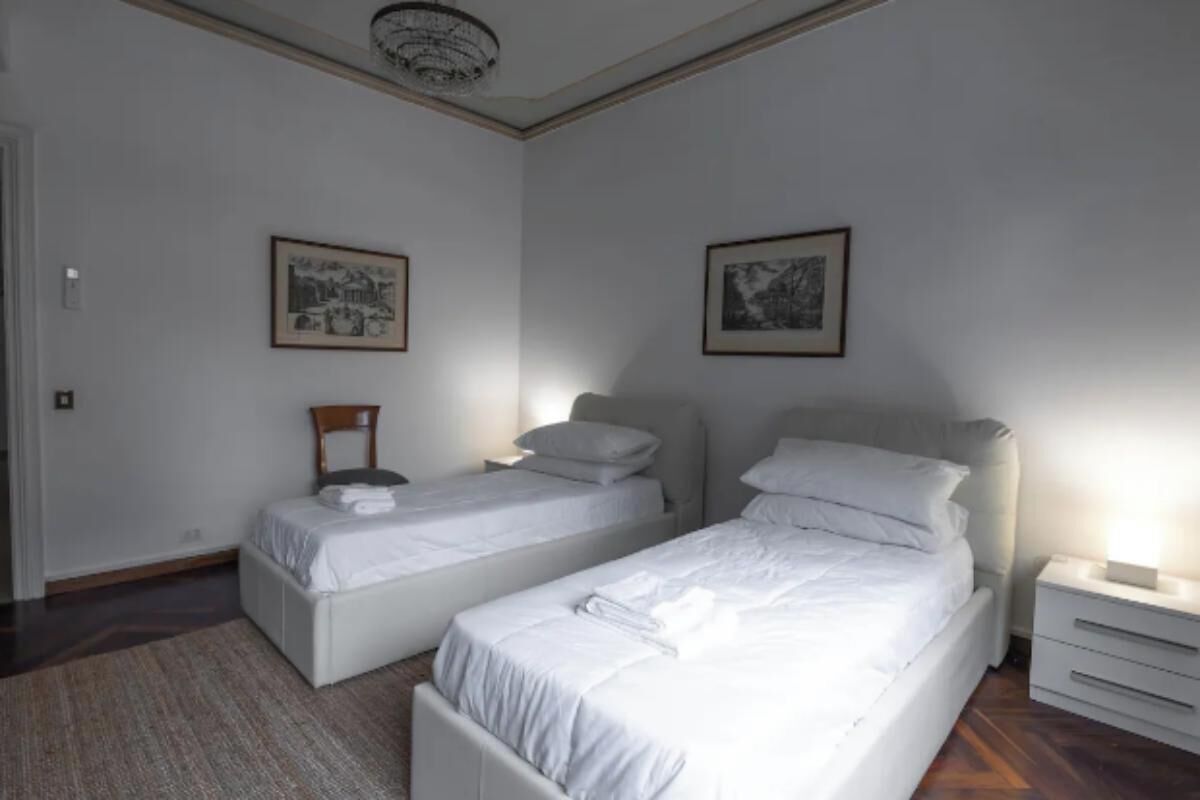 Una camera da letto con due letti singoli, un comodino con una lampada e due quadri appesi al muro.