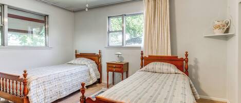 A bedroom with two wooden beds, a ceiling fan, a window with curtains, and a small bedside table with a lamp.