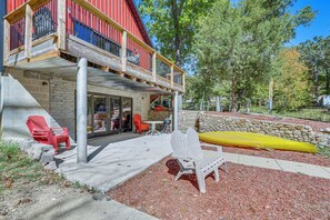 A wooden deck with Adirondack chairs, a kayak, and a stone wall.