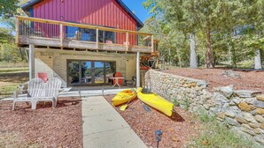 En röd byggnad med en balkong, kajaker och Adirondack-stolar.
