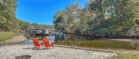 Vista sobre un lago con un muelle, dos sillas Adirondack rojas y un edificio al otro lado del agua.