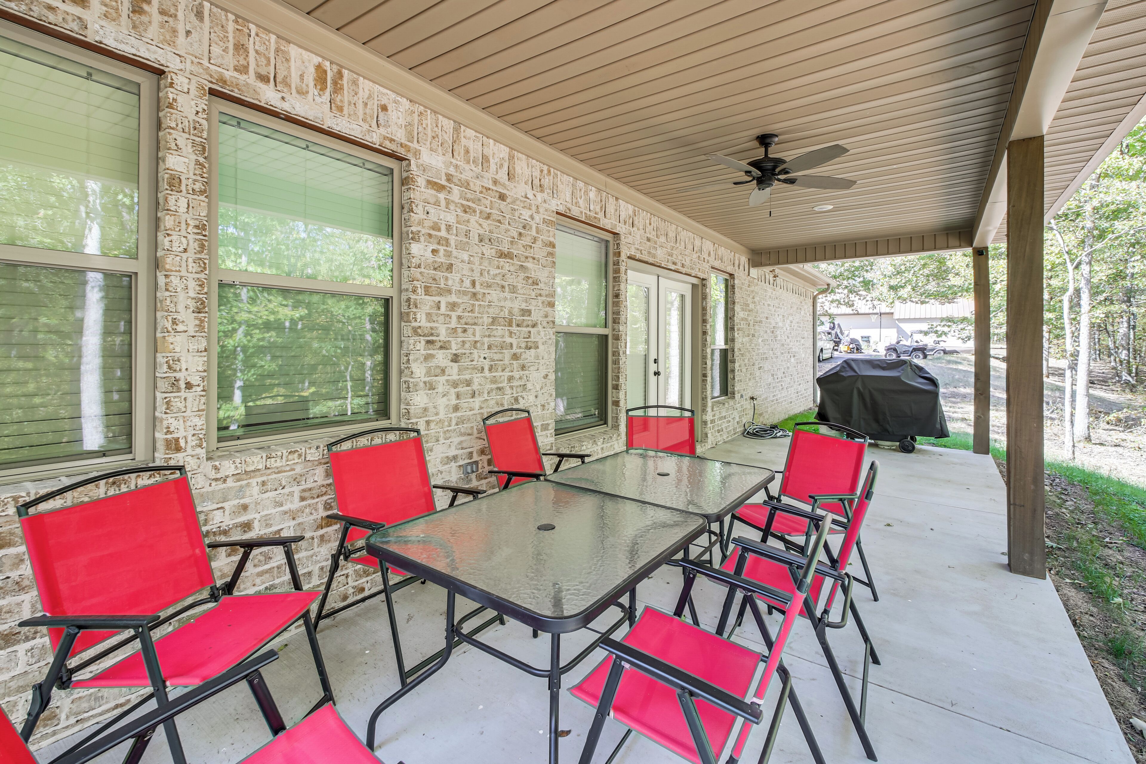 A covered patio with a brick wall, a glass table, red chairs, and a ceiling fan.