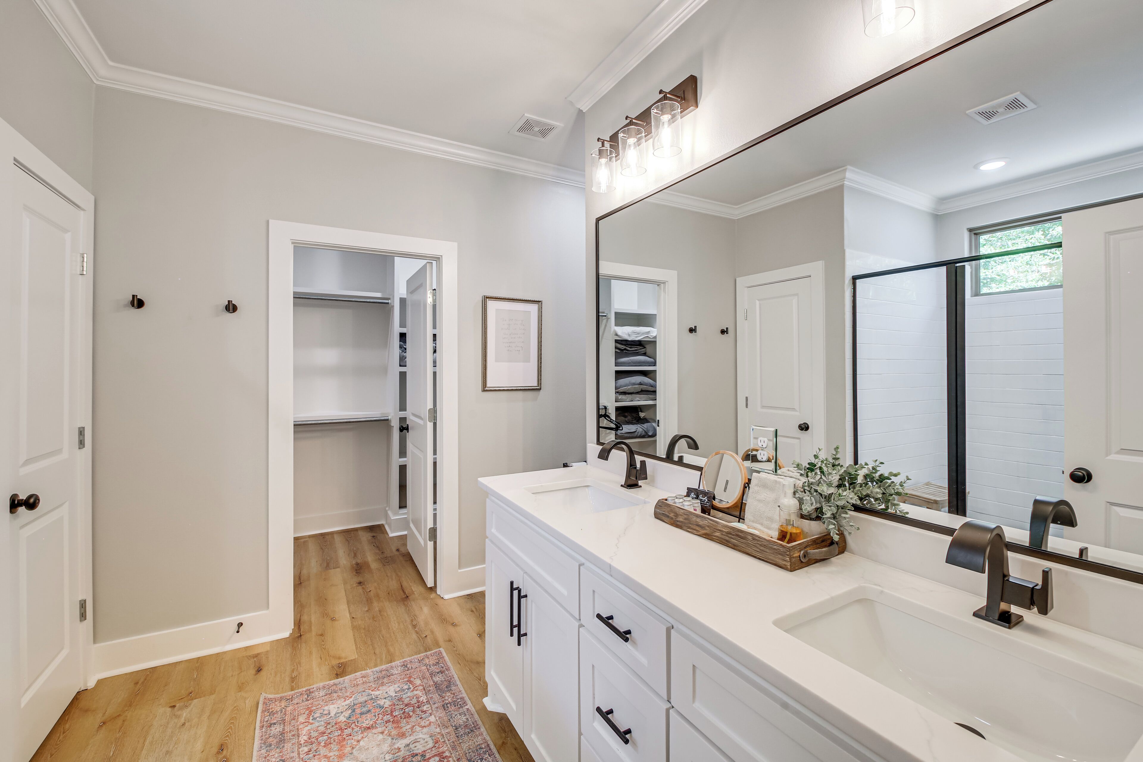 A modern bathroom with a large mirror, white vanity, and a walk-in closet.