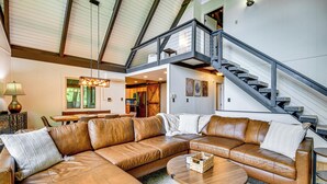 A spacious living area with a large leather sectional sofa, a round coffee table, and a staircase leading to an upper level. - Blue Ridge Pkwy View & Deck: Brevard Home! (Brevard)