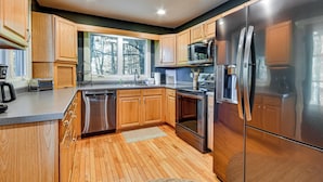 A modern kitchen with wooden cabinets, stainless steel appliances, and a large window. - Blue Ridge Pkwy View & Deck: Brevard Home! (Brevard)