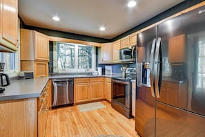 A modern kitchen with wooden cabinets, stainless steel appliances, and a large window. - Blue Ridge Pkwy View & Deck: Brevard Home! (Brevard)