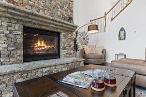 Una sala de estar con chimenea de piedra, una mesa de centro con revistas y vasos, un sofá y una escalera.