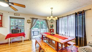 Un espace repas comprenant une table en bois, des bancs, un ventilateur de plafond et une vue sur l’extérieur grâce à de grandes fenêtres.