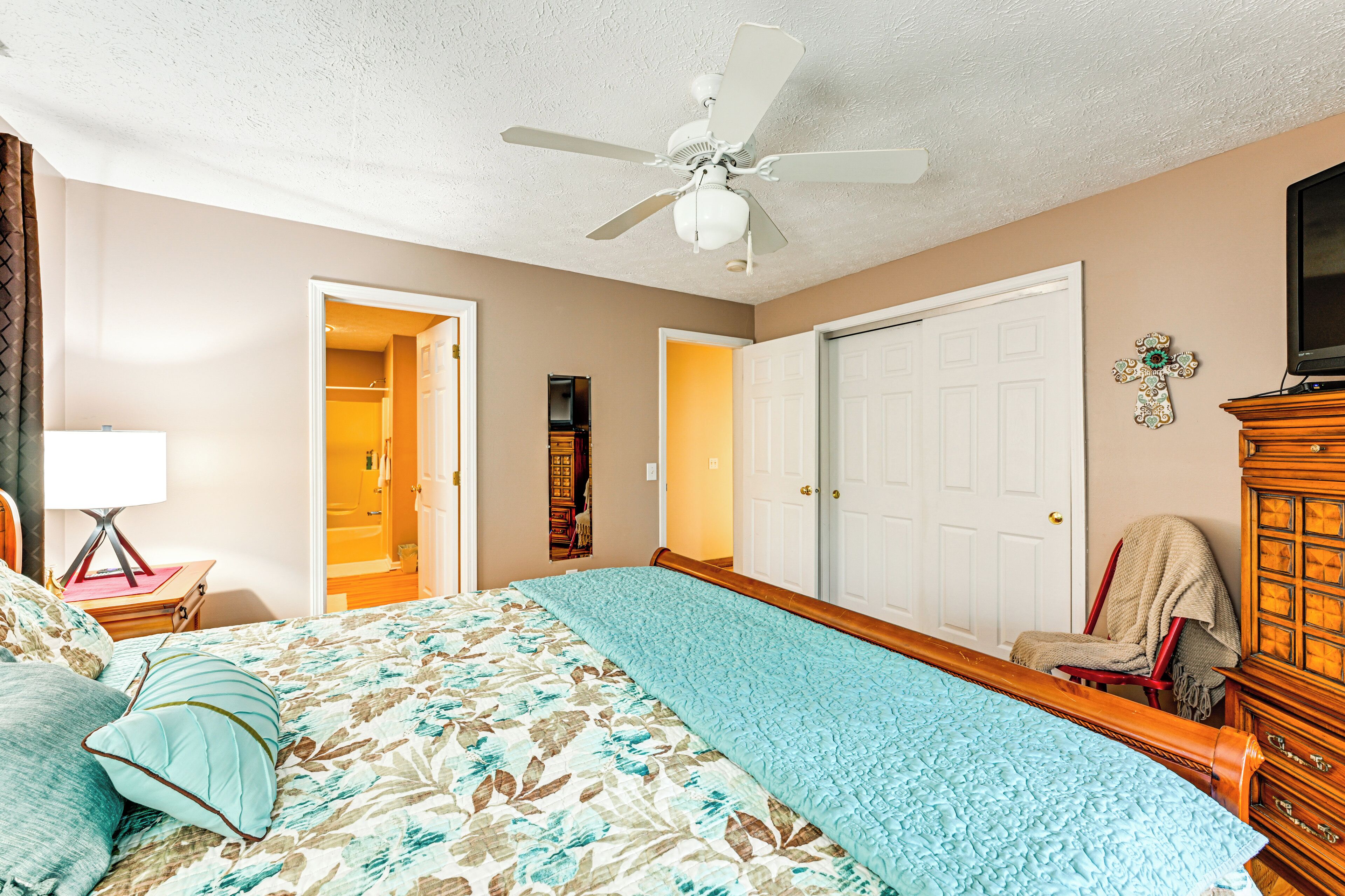 A bedroom with a bed, a ceiling fan, a TV, and a wooden dresser.