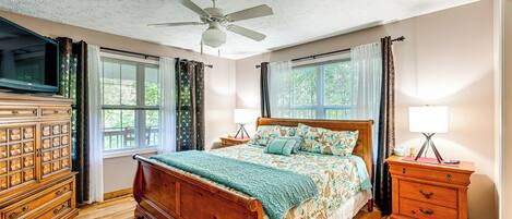 A bedroom with a wooden bed, a nightstand, a dresser, a ceiling fan, and windows with curtains.
