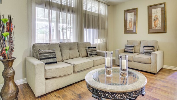 A living room with two beige sofas, a round coffee table with decorative items, and a vase with plants. - Family-friendly Home w/ Fenced Yard in Victorville (Victorville)