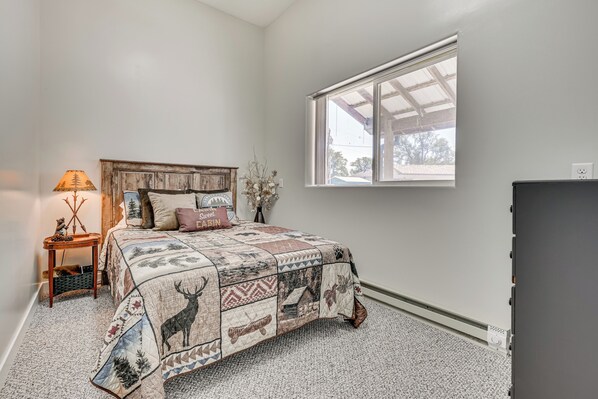 A bedroom with a wooden headboard, a quilted bedspread, a nightstand with a lamp, and a window with a view of the outdoors.