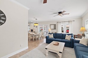 A living room with a blue sofa, a coffee table, and a ceiling fan. - Gulf Side Gated Comm with Beach Access- Fintastic by Royal Destinations (Santa Rosa Beach)