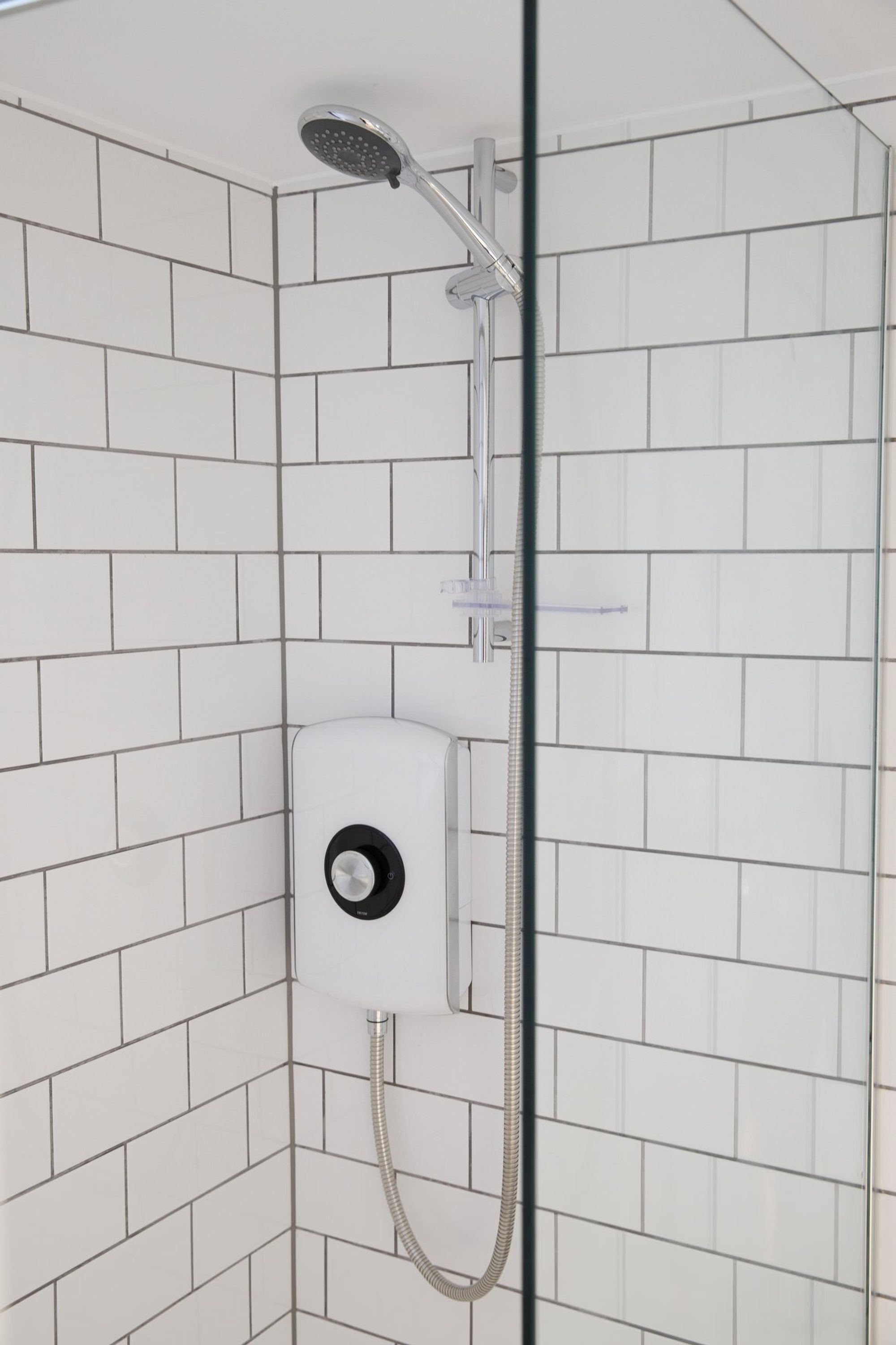 A shower area with white tiled walls and a handheld showerhead.