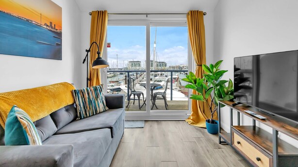 A modern living room with a sofa, TV, and balcony overlooking a marina. - On the Water 5 With Free Parking By My Getaways (Brighton)