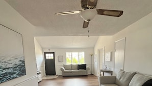 Amplia sala de estar con piso de madera, ventilador de techo, sofá y un ventanal grande.