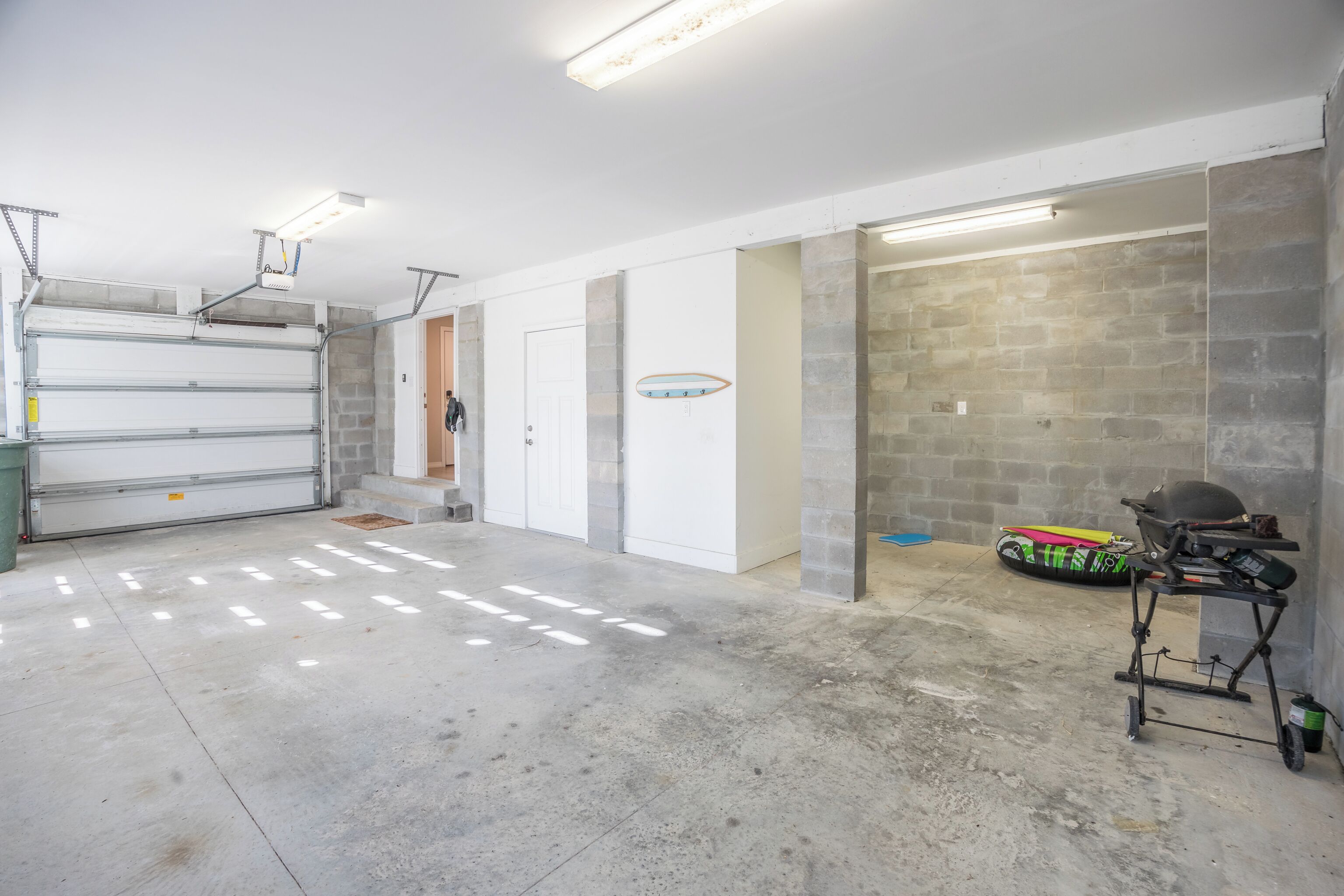 A garage with a concrete floor, a white garage door, and a motorcycle in the background.