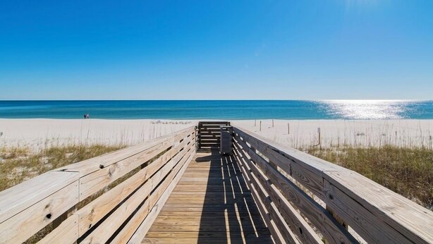A wooden boardwalk leading to a beach with clear skies and calm waters.
