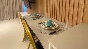 Ein moderner Essbereich mit einem langen Tisch, gedeckt für zwei Personen, mit hellem Tischlauf, passenden Unterlagen und einem blauen Teekännchen.