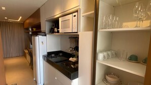 Eine moderne Küche mit weißen Schränken, einer schwarzen Arbeitsplatte und einer eingebauten Mikrowelle. Auf den Regalen stehen Weingläser und Teller, und auf der Arbeitsplatte steht eine Kaffeemaschine.