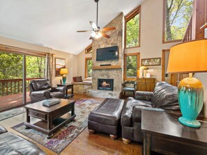 A spacious living room with a stone fireplace, leather furniture, and large windows offering a view of the outdoors.