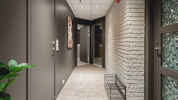 Un pasillo con piso de baldosas, pared de ladrillo y una puerta con panel de vidrio.