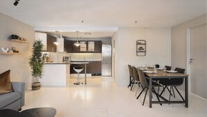 Una cocina moderna con armarios blancos, una isla central y un comedor con mesa y sillas de madera.