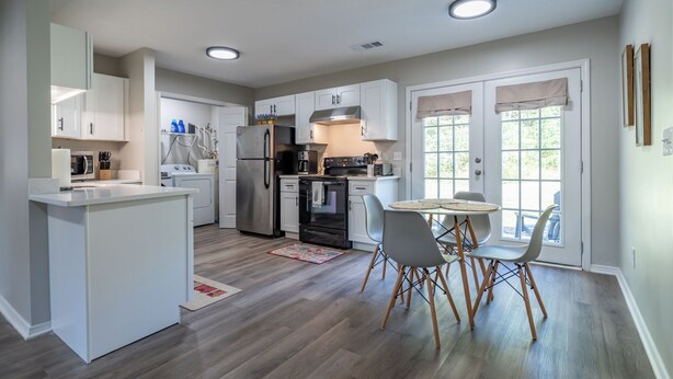A modern kitchen with white cabinetry, a stainless steel refrigerator, a built-in oven, and a dining area with a table and chairs. - Extended Stay 2BR • Relocation Friendly (Calhoun)