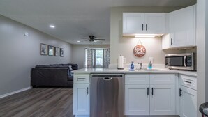A modern kitchen with white cabinets, a dishwasher, a microwave, and a ceiling fan. - Extended Stay 2BR • Relocation Friendly (Calhoun)