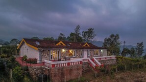 A two-story house with a stone foundation, a red brick lower level, and a white upper level with yellow trim. - Rico Retreat (Kotagiri)