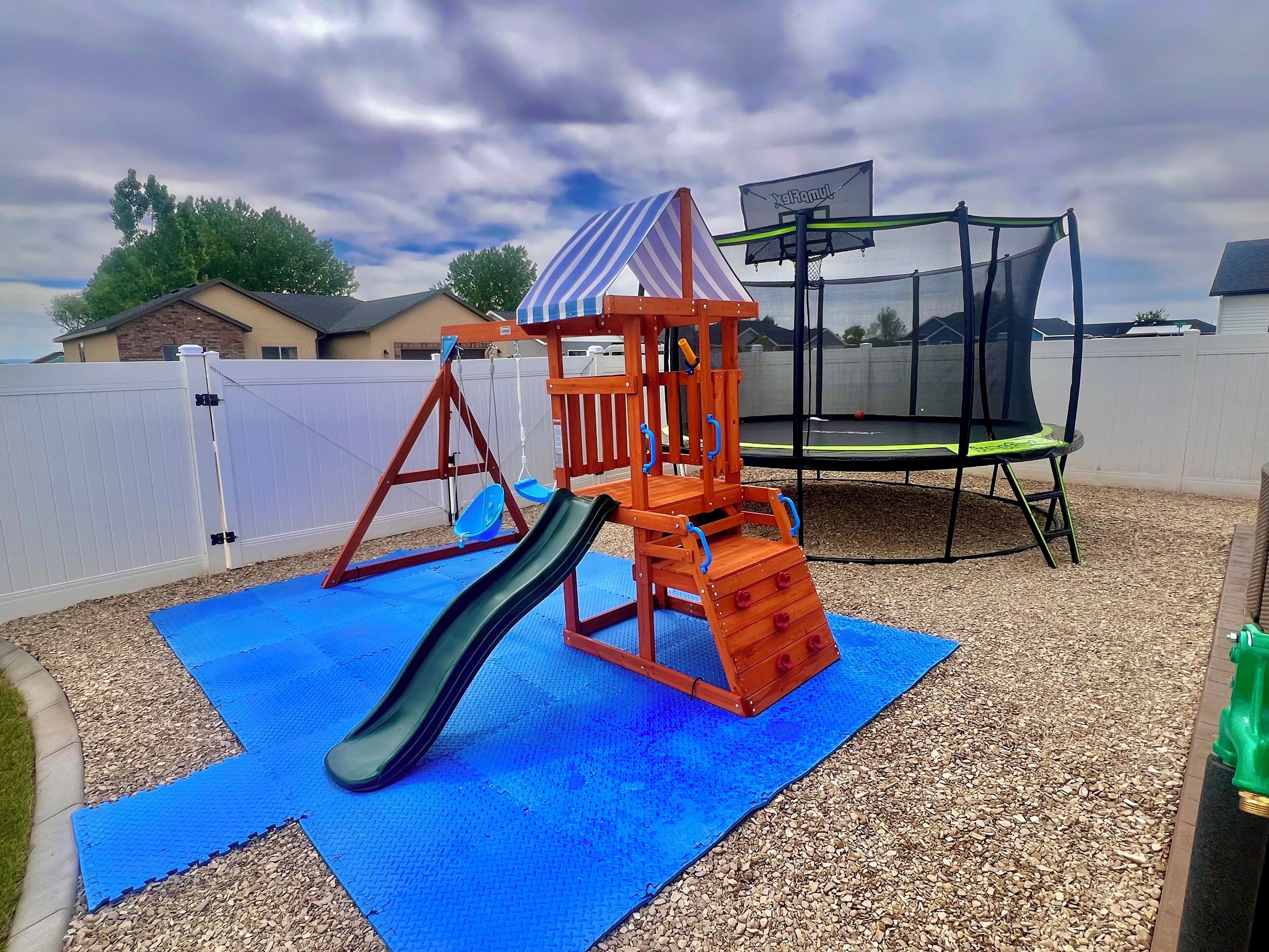 A playground with a slide and swings, a trampoline, and a covered play structure.