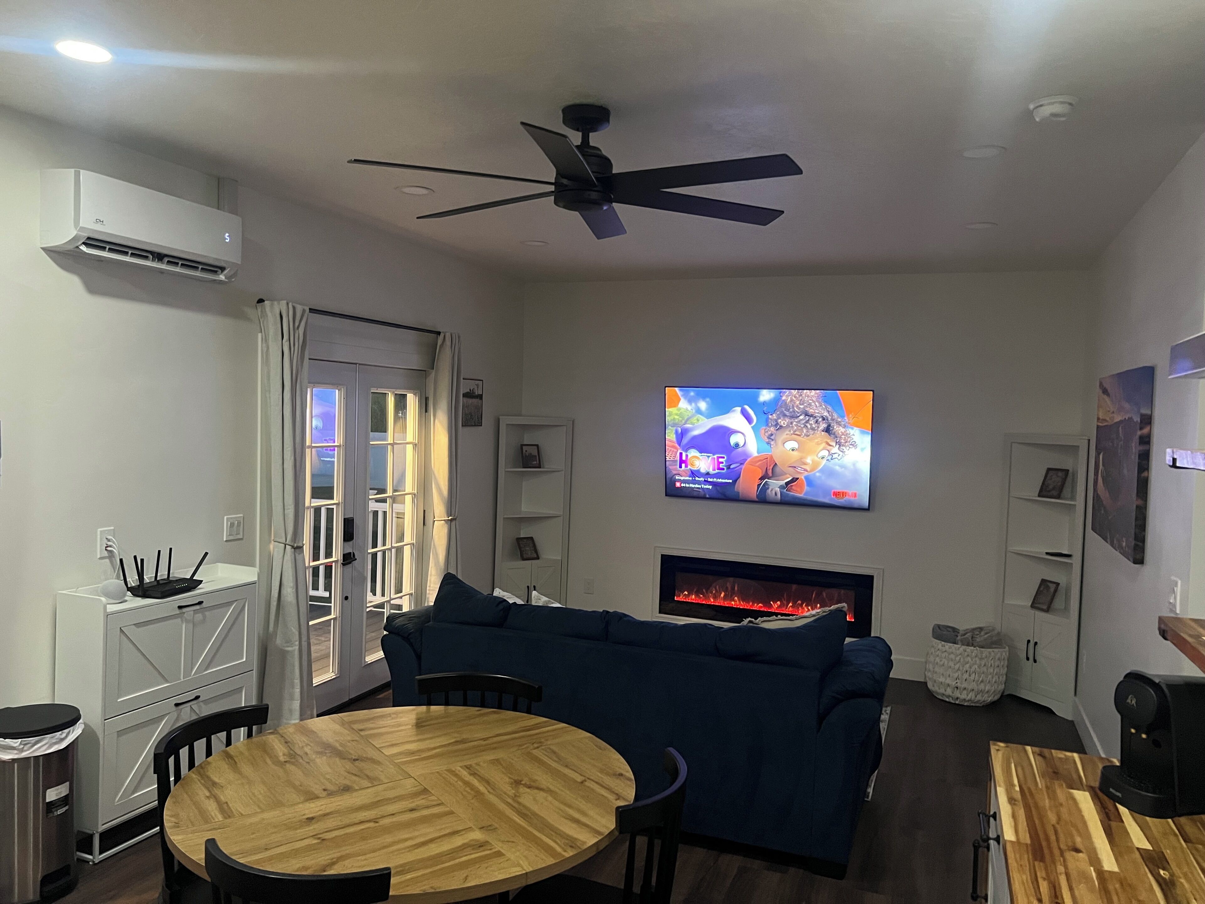 A modern living room with a blue sofa, a wooden dining table, and a flat-screen TV mounted on the wall.