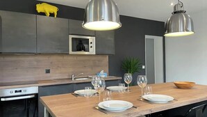 Una cocina moderna con una mesa de comedor de madera preparada para cuatro personas, electrodomésticos de acero inoxidable e iluminación colgante.