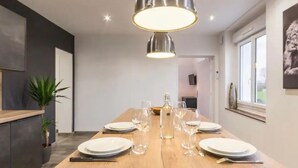 Comedor con mesa de madera preparada para cuatro, una lámpara colgante y vistas de la habitación contigua.