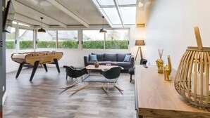 Una sala de estar moderna con una mesa de centro de madera, sillas negras, un sofá gris y una mesa de fútbol.