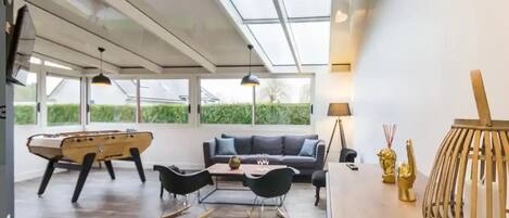 A modern living room with a wooden coffee table, black chairs, a gray sofa, and a foosball table.